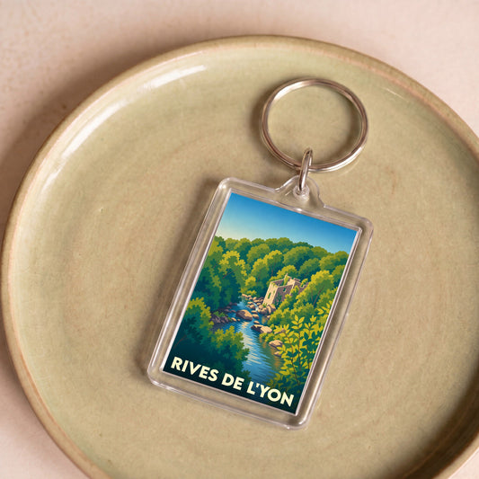 Porte-clés souvenir de la ville de Rives de l'Yon avec une illustration stylisée d'un paysage de rivière et de forêt.
