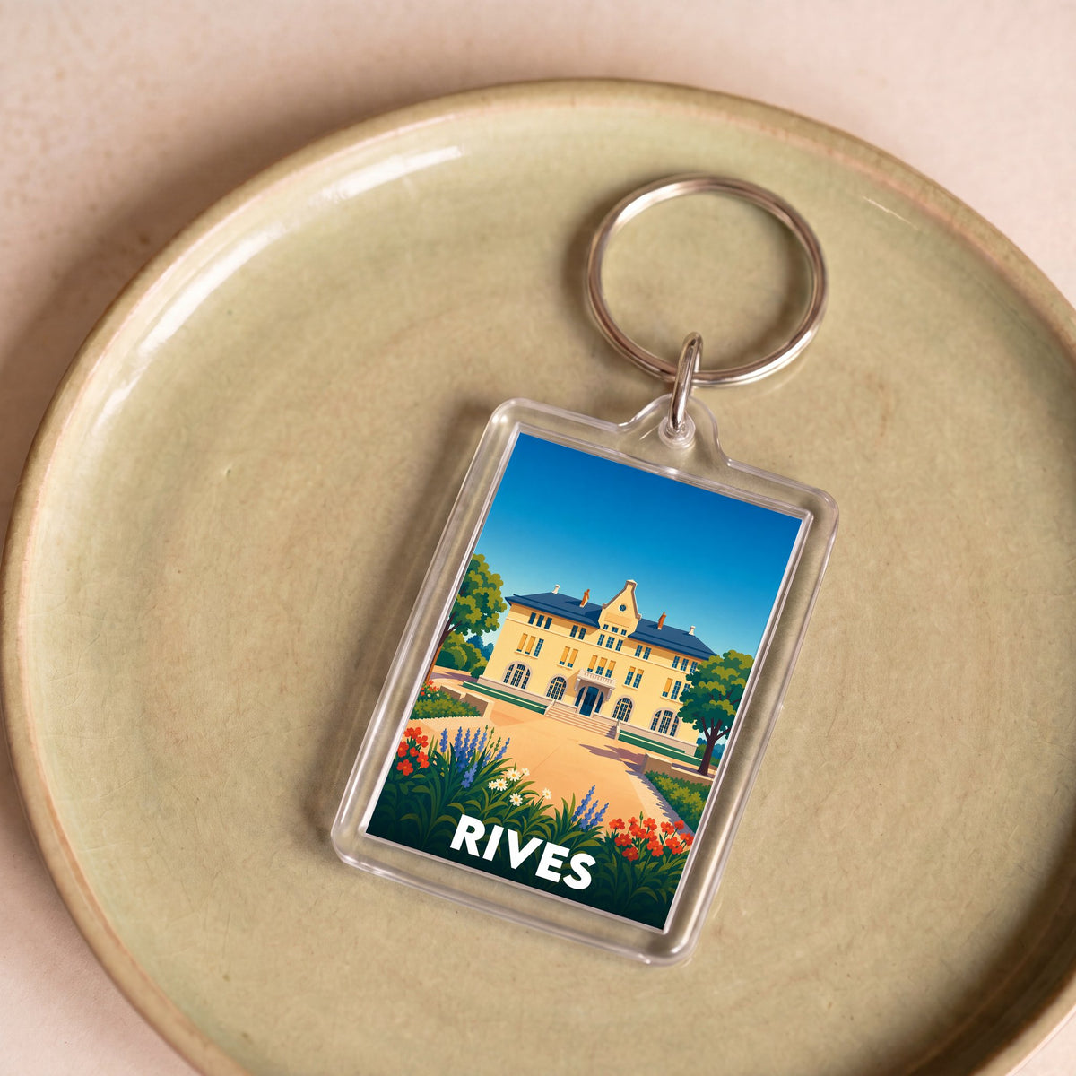 Porte-clés souvenir de la ville de Rives avec une illustration stylisée d'une grande demeure et de son jardin.