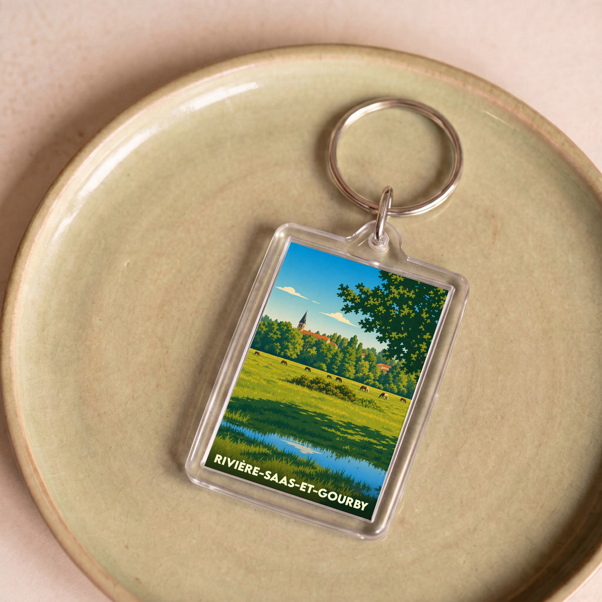 Porte-clés souvenir de la ville de Rivière-Saas-et-Gourby avec une illustration stylisée de son paysage champêtre.