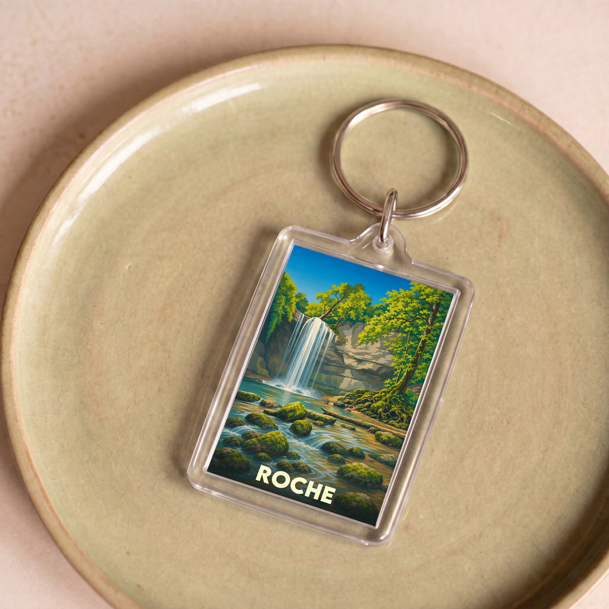 Porte-clés souvenir de la ville de Roche avec une illustration stylisée d'une cascade en forêt.