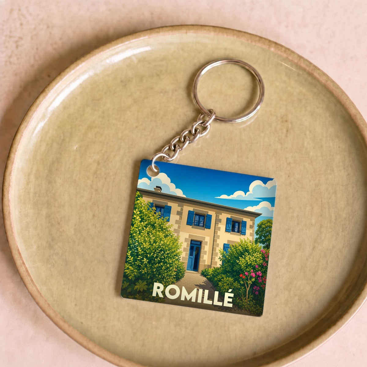 Porte-clés souvenir de la ville de Romillé avec une illustration stylisée d'une maison régionale.