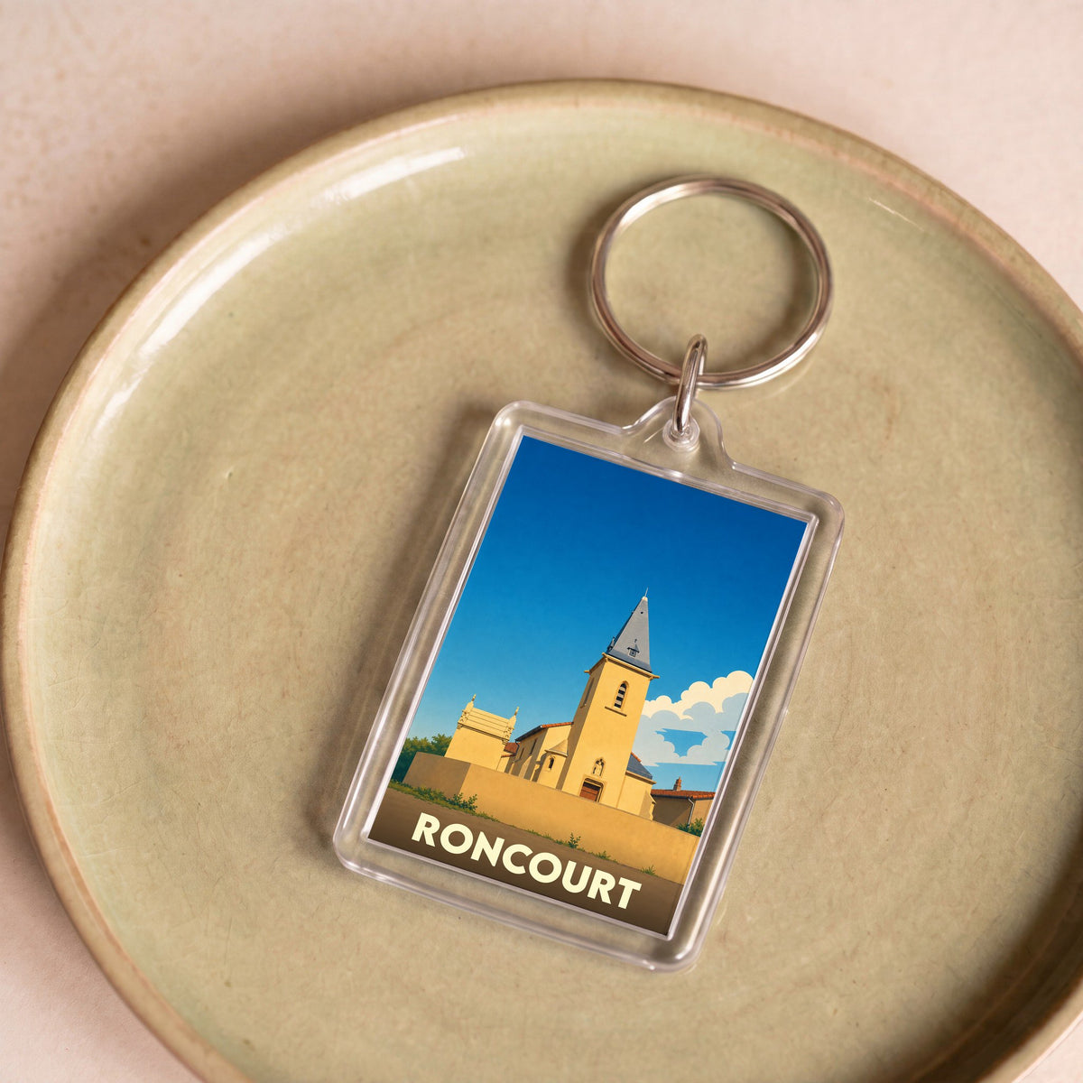 Porte-clés souvenir de la ville de Roncourt avec une illustration stylisée d'une église sous un ciel bleu.