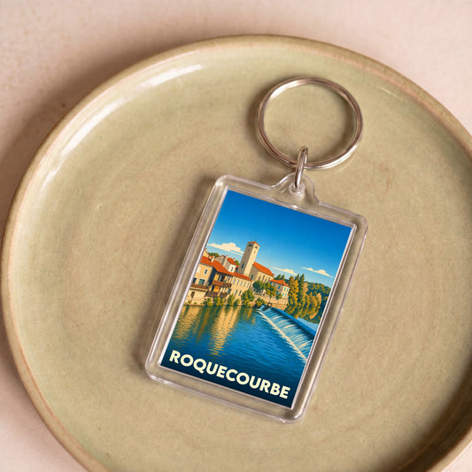 Porte-clés souvenir de la ville de Roquecourbe avec une illustration stylisée d'un paysage urbain au bord de l'eau.