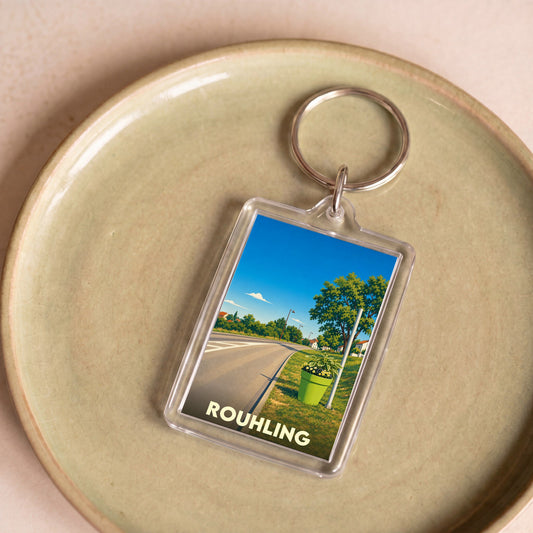 Porte-clés souvenir de la ville de Rouhling avec une illustration stylisée d'un paysage routier ensoleillé.