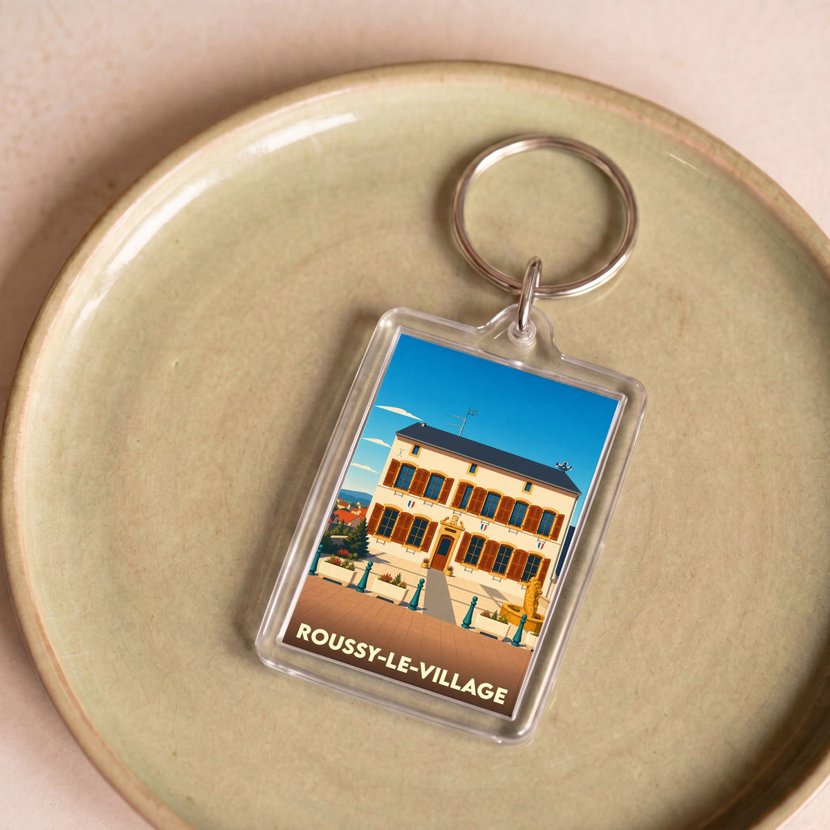 Porte-clés souvenir de la ville de Roussy-le-Village avec une illustration stylisée de sa mairie.