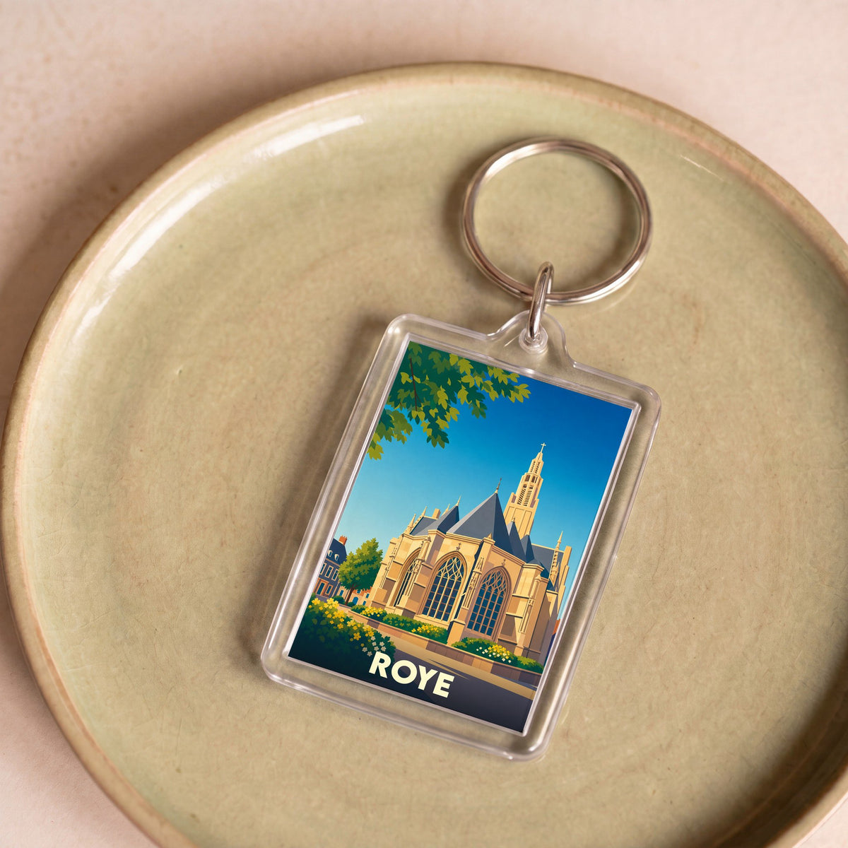 Porte-clés souvenir de la ville de Roye avec une illustration stylisée d'une église sous un ciel bleu.