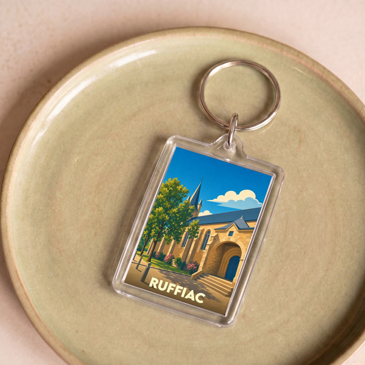 Porte-clés souvenir de la ville de Ruffiac avec une illustration stylisée d'une église sous un ciel bleu.