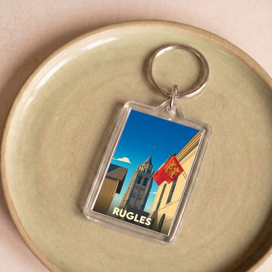 Porte-clés souvenir de la ville de Rugles avec une illustration stylisée de son clocher et du drapeau normand.