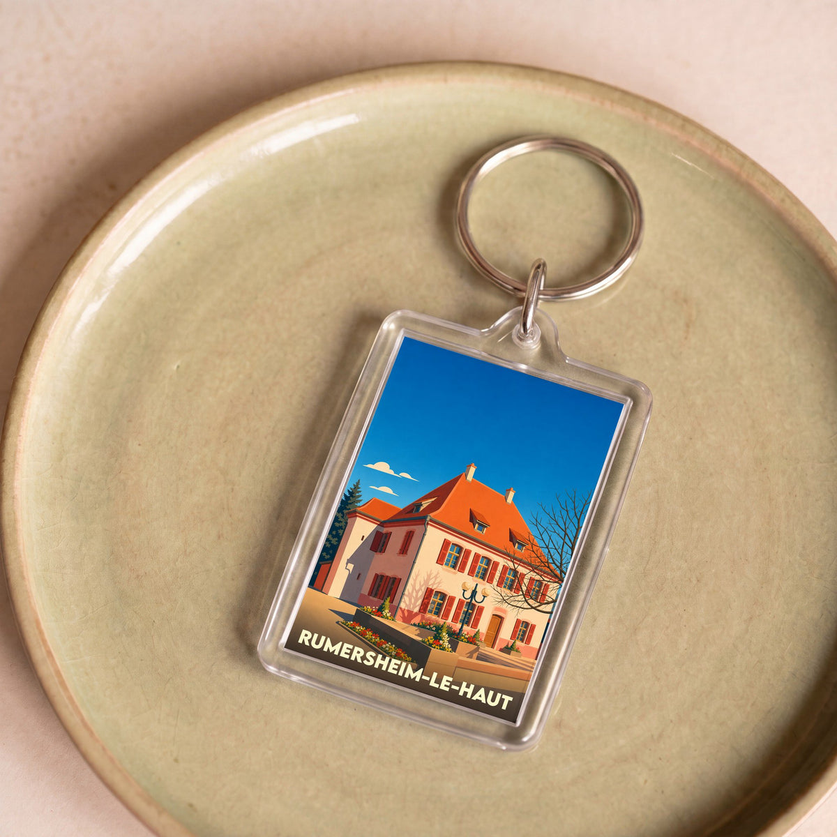 Porte-clés souvenir de la ville de Rumersheim-le-Haut avec une illustration stylisée d'un bâtiment traditionnel.
