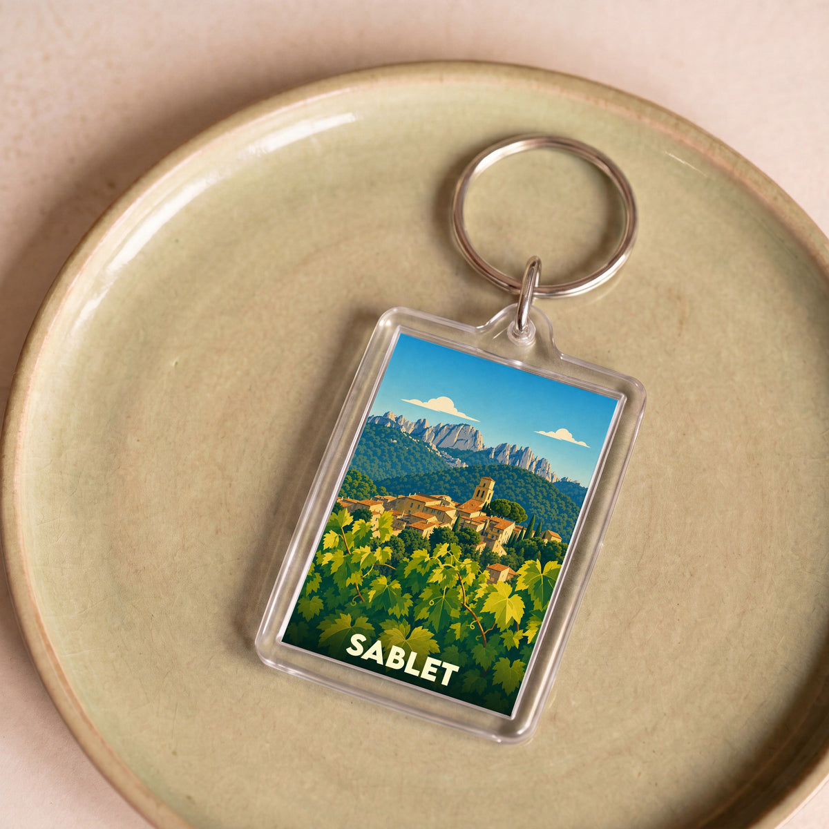 Porte-clés souvenir de la ville de Sablet avec une illustration stylisée d'un vignoble et d'un village provençal.