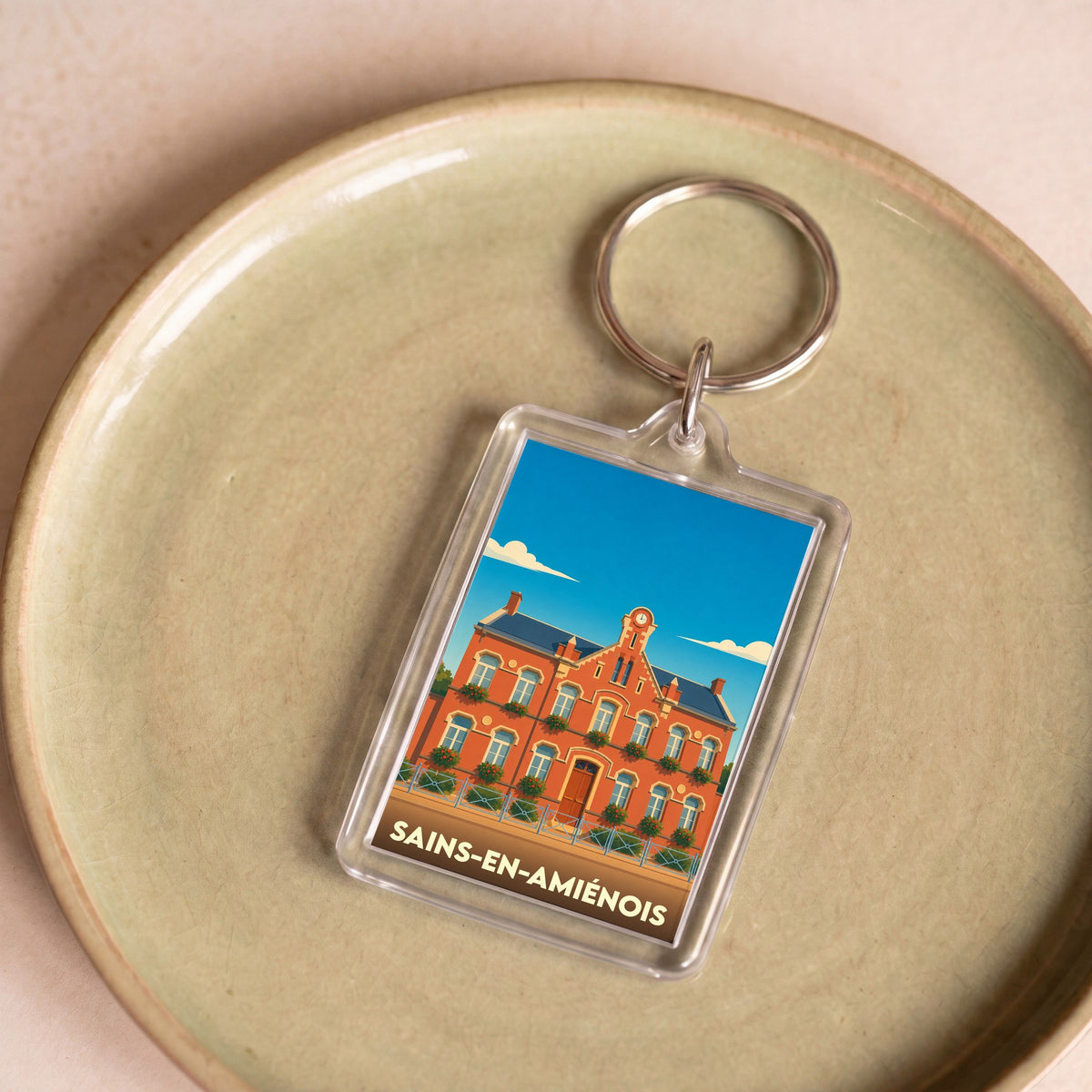 Porte-clés souvenir de la ville de Sains-en-Amiénois avec une illustration stylisée de sa mairie.