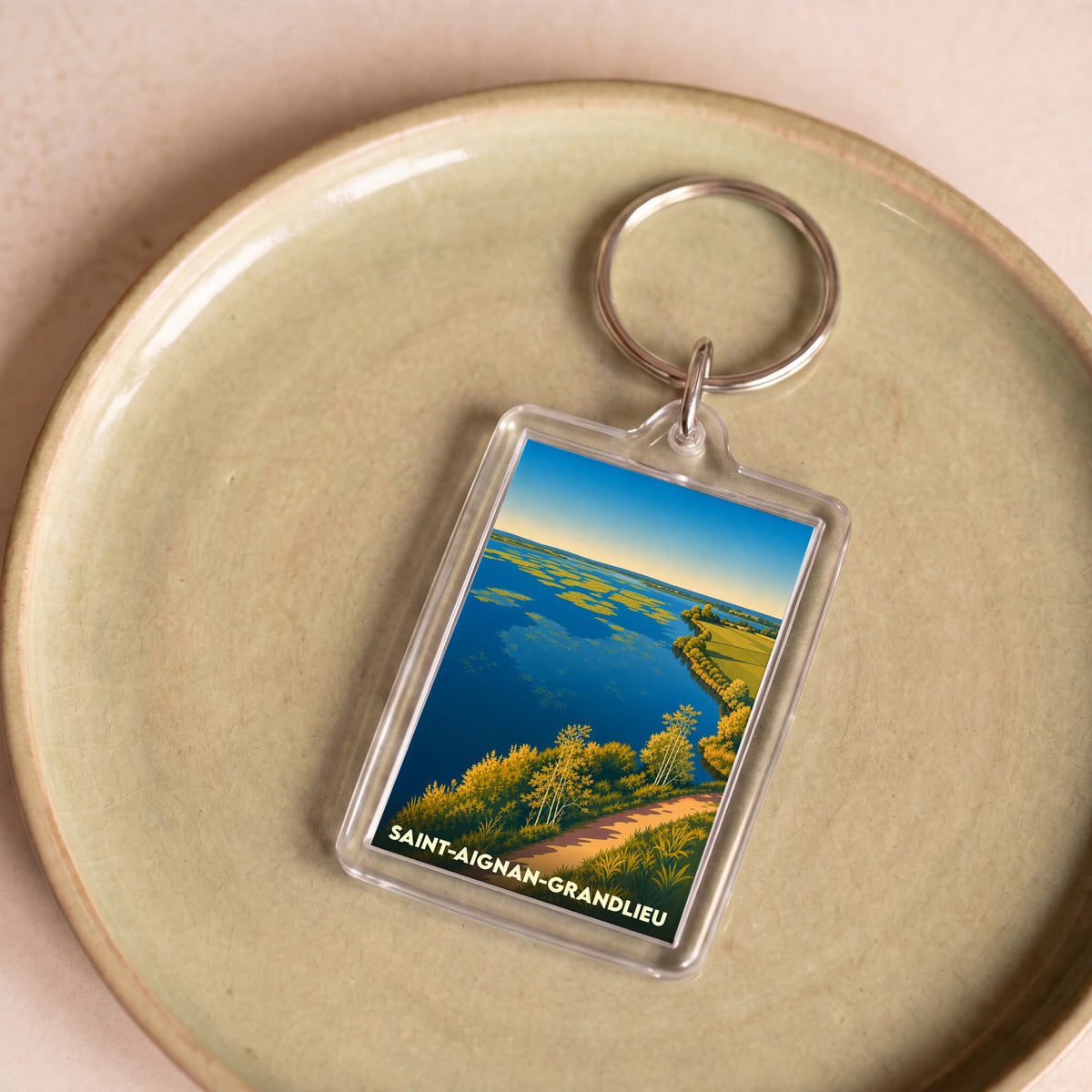 Porte-clés souvenir de la ville de Saint-Aignan-Grandlieu avec une illustration stylisée d'un lac bordé de végétation.