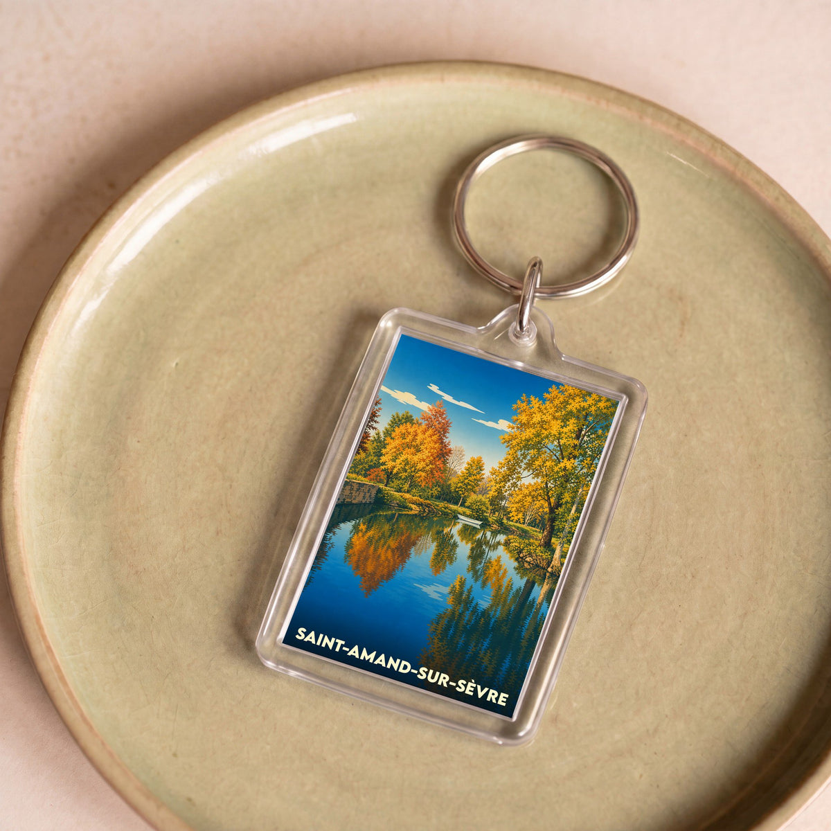 Porte-clés souvenir de la ville de Saint-Amand-sur-Sèvre illustré par un paysage d'automne se reflétant dans l'eau.