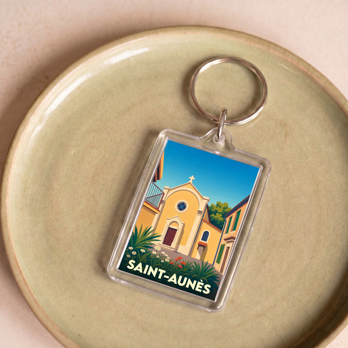 Porte-clés souvenir de la ville de Saint-Aunès avec une illustration stylisée d'une église sous un ciel bleu.