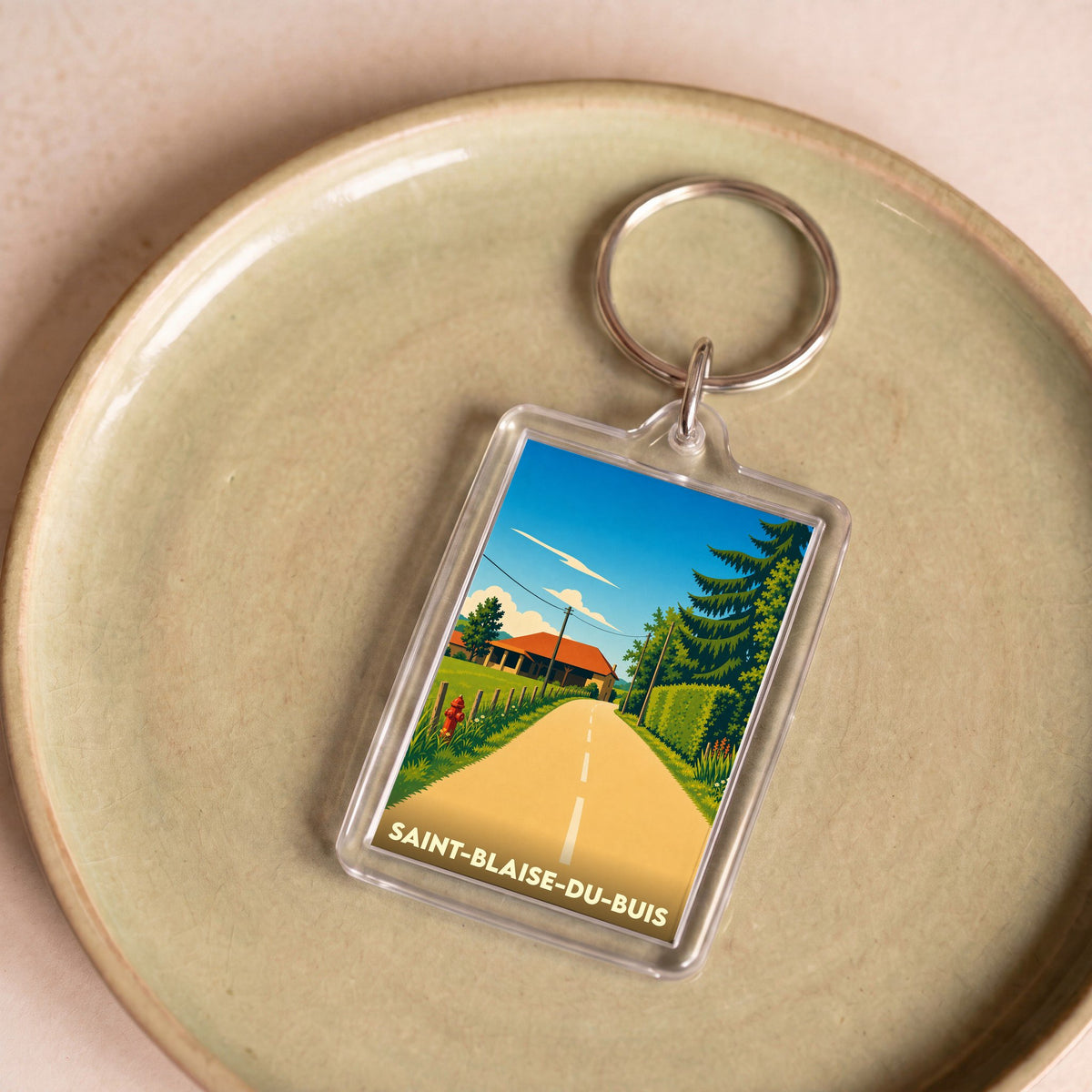 Porte-clés souvenir de la ville de Saint-Blaise-du-Buis avec une illustration stylisée d'un paysage rural.