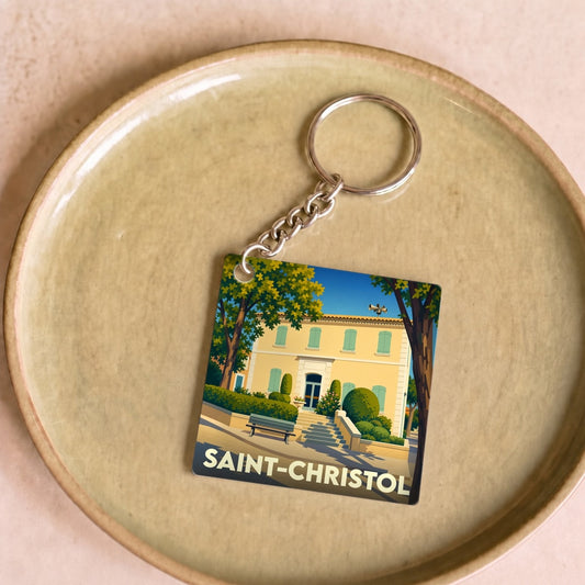 Porte-clés souvenir de la ville de Saint-Christol avec une illustration stylisée d'une bastide provençale.