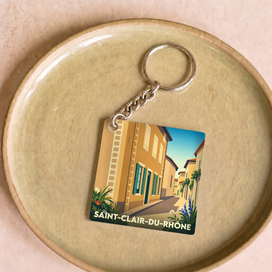 Porte-clés souvenir de la ville de Saint-Clair-du-Rhône avec une illustration stylisée d'une ruelle ensoleillée.