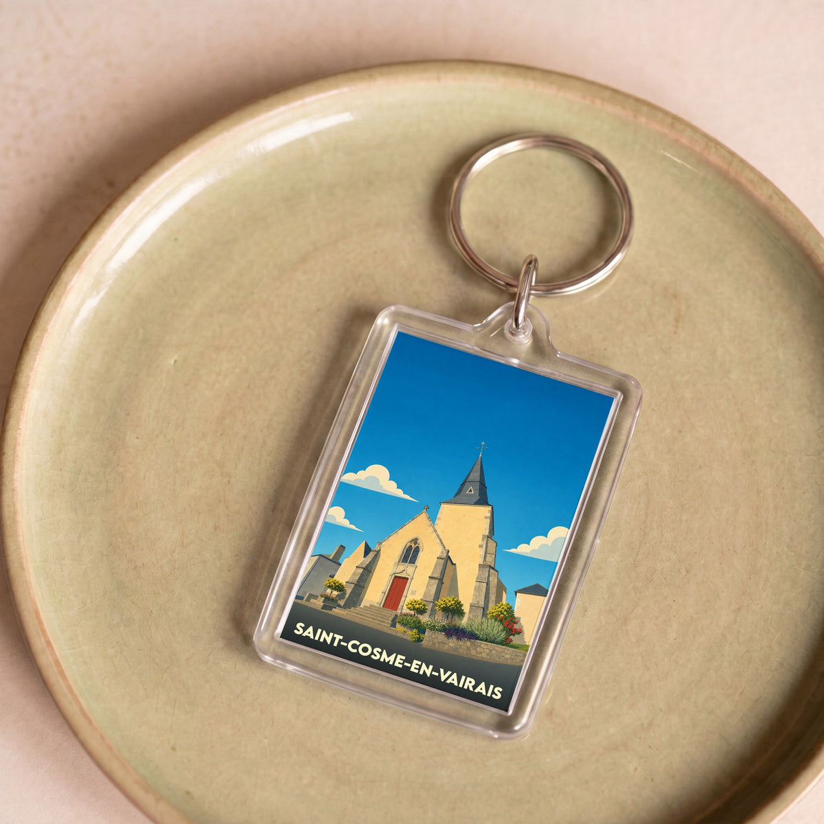 Porte-clés souvenir de la ville de Saint-Cosme-en-Vairais avec une illustration stylisée de son église.