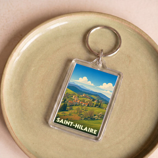 Porte-clés souvenir de la ville de Saint-Hilaire avec une illustration stylisée de paysages vallonnés.