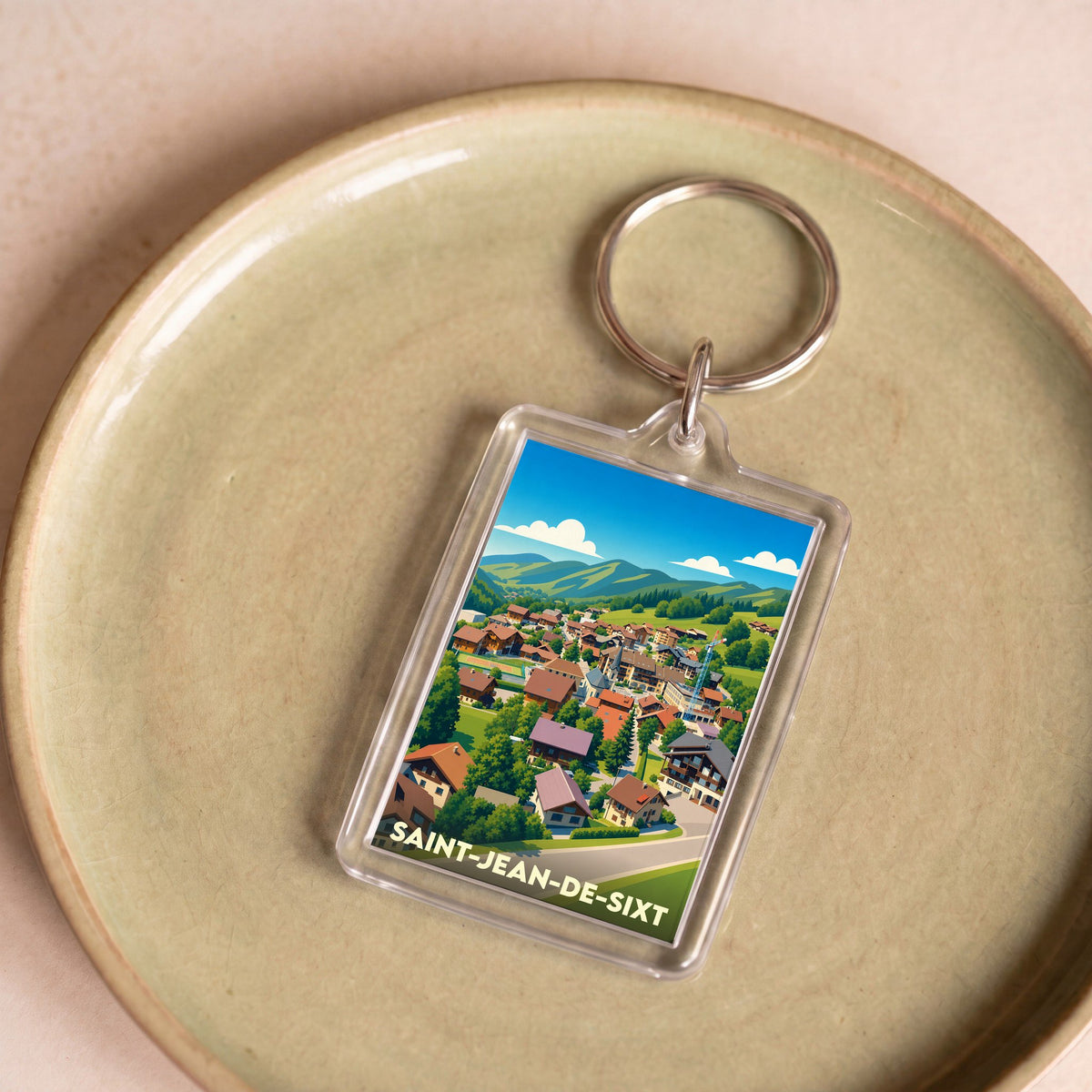 Porte-clés souvenir de la ville de Saint-Jean-de-Sixt avec une illustration stylisée d'un village de montagne.