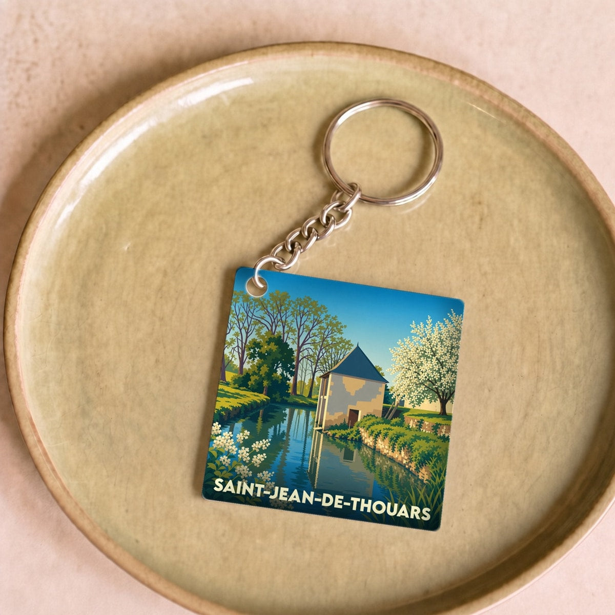 Porte-clés souvenir de la ville de Saint-Jean-de-Thouars avec une illustration stylisée d'un paysage de bord de rivière.
