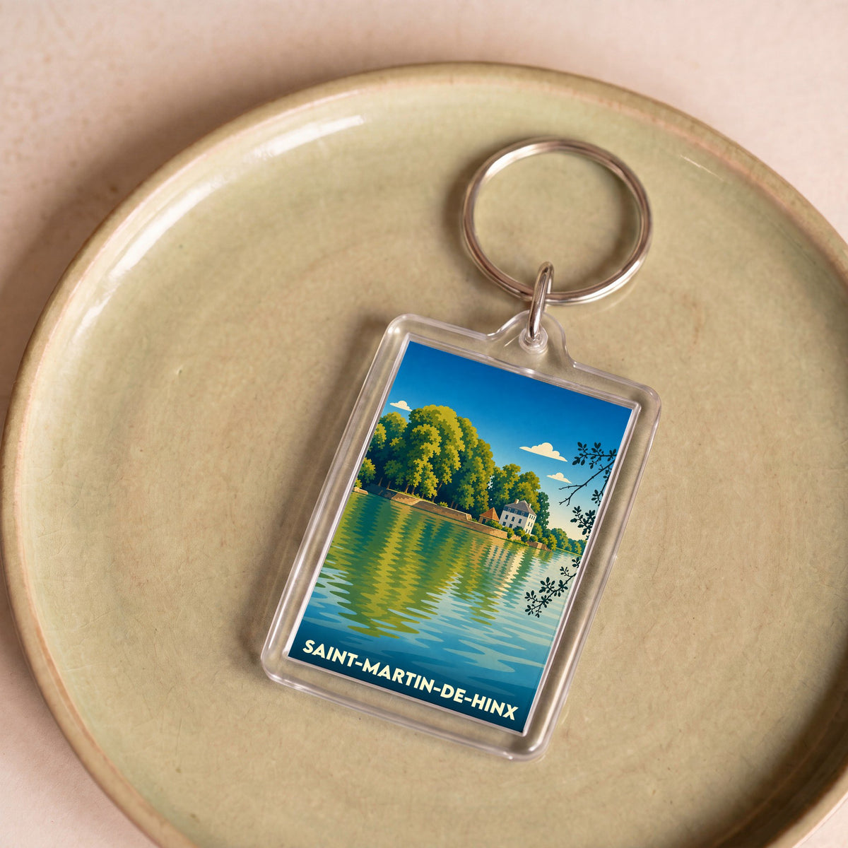Porte-clés souvenir de la ville de Saint-Martin-de-Hinx avec une illustration stylisée d'un paysage de bord d'eau.