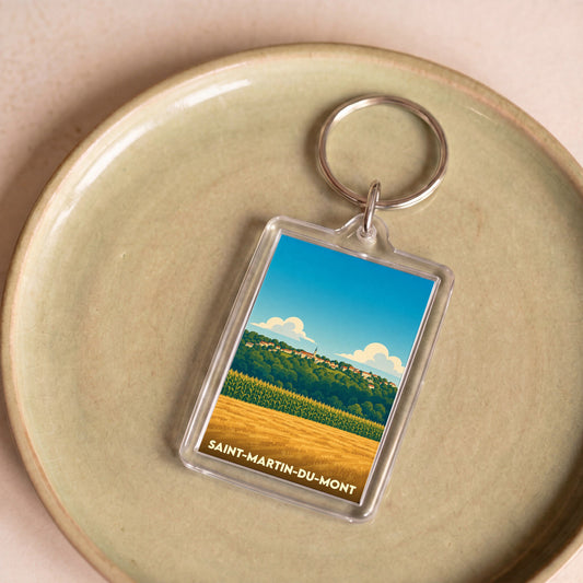 Porte-clés souvenir de la ville de Saint-Martin-du-Mont avec une illustration stylisée de paysages ruraux.