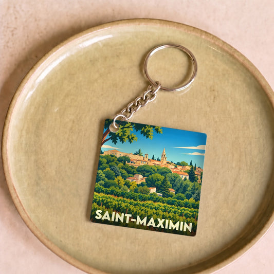 Porte-clés souvenir de la ville de Saint-Maximin avec une illustration stylisée d'un village provençal niché dans la verdure.