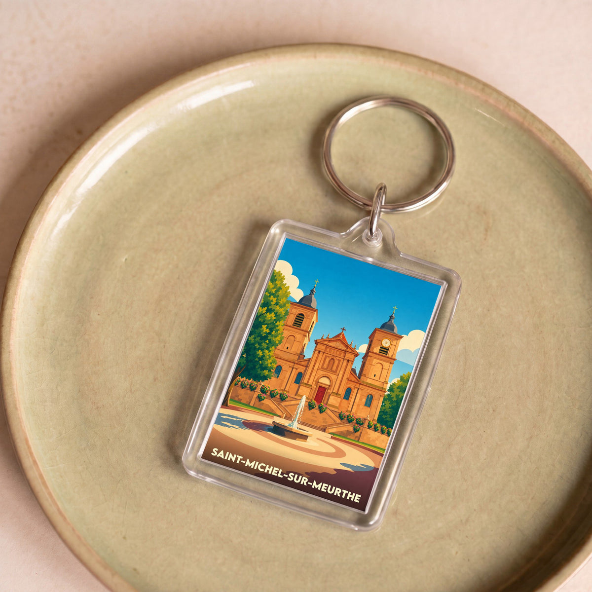Porte-clés souvenir de la ville de Saint-Michel-sur-Meurthe avec une illustration stylisée de son église et d'une fontaine.