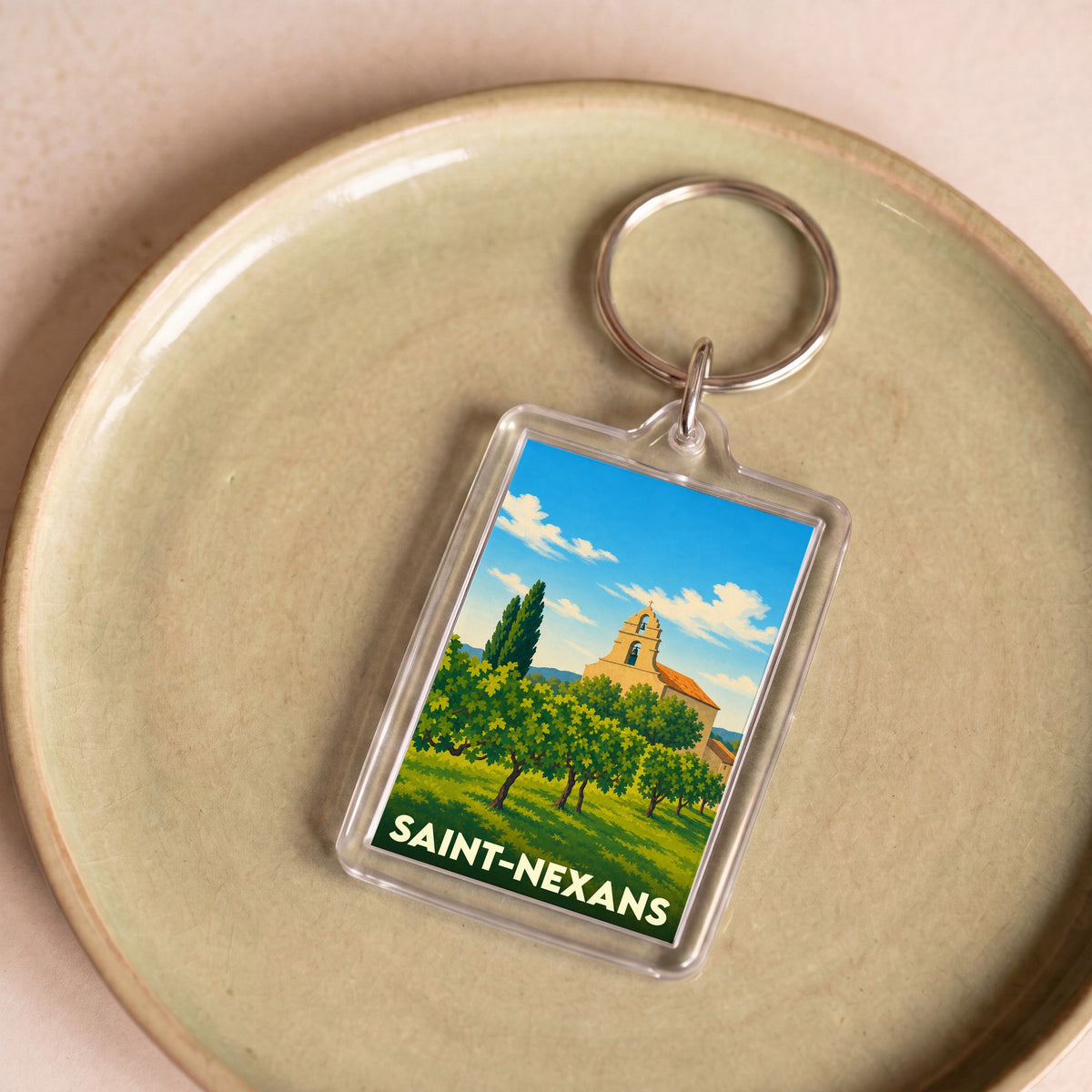 Porte-clés souvenir de la ville de Saint-Nexans avec une illustration stylisée d'un paysage ensoleillé.