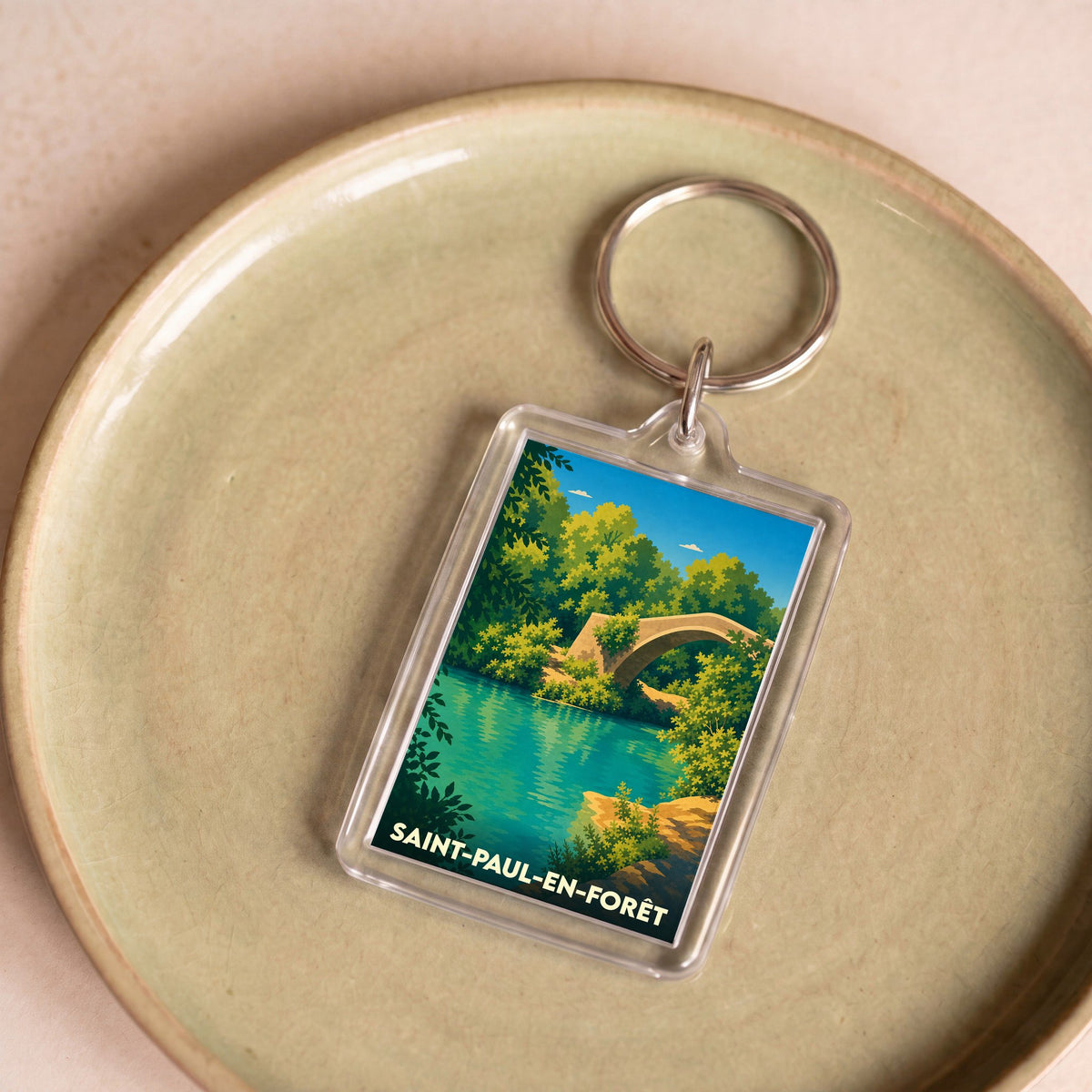 Porte-clés souvenir de la ville de Saint-Paul-en-Forêt avec une illustration stylisée d'un pont en pierre bordé de verdure.