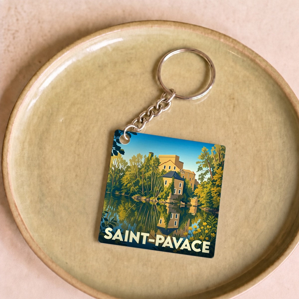 Porte-clés souvenir de la ville de Saint-Pavace avec une illustration stylisée d'un manoir se reflétant dans l'eau.