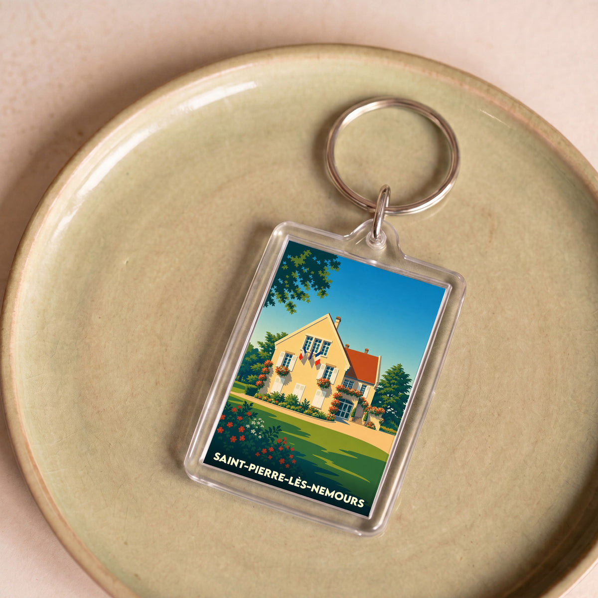 Porte-clés souvenir de la ville de Saint-Pierre-lès-Nemours avec une illustration stylisée d'une maison fleurie.