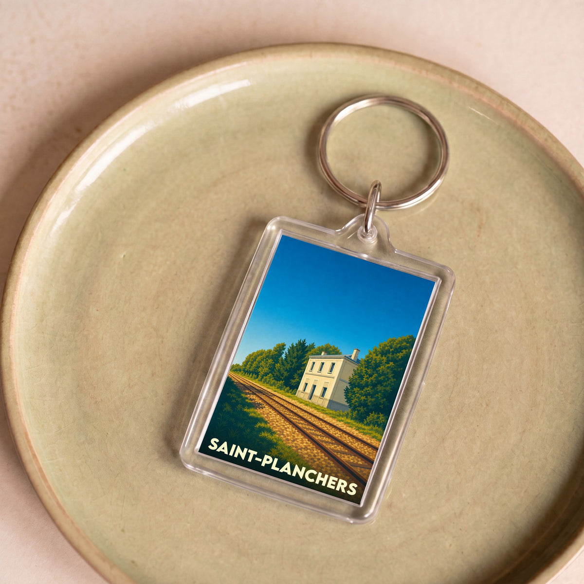 Porte-clés souvenir de la ville de Saint-Planchers illustrant une ancienne gare le long d'une voie ferrée.