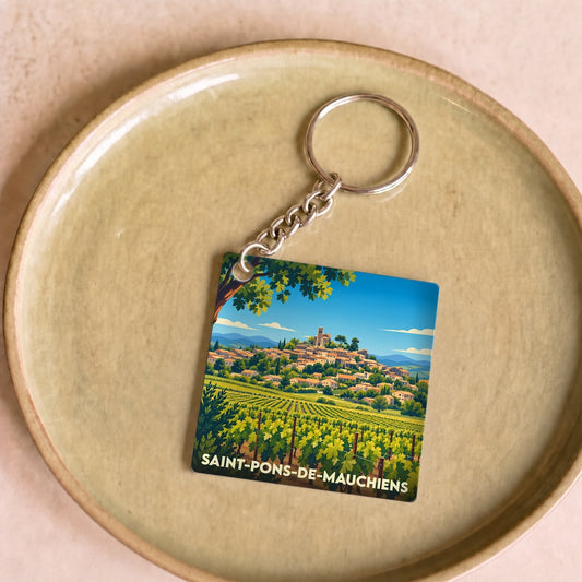 Porte-clés souvenir de la ville de Saint-Pons-de-Mauchiens avec une illustration stylisée d'un vignoble et d'un village perché.