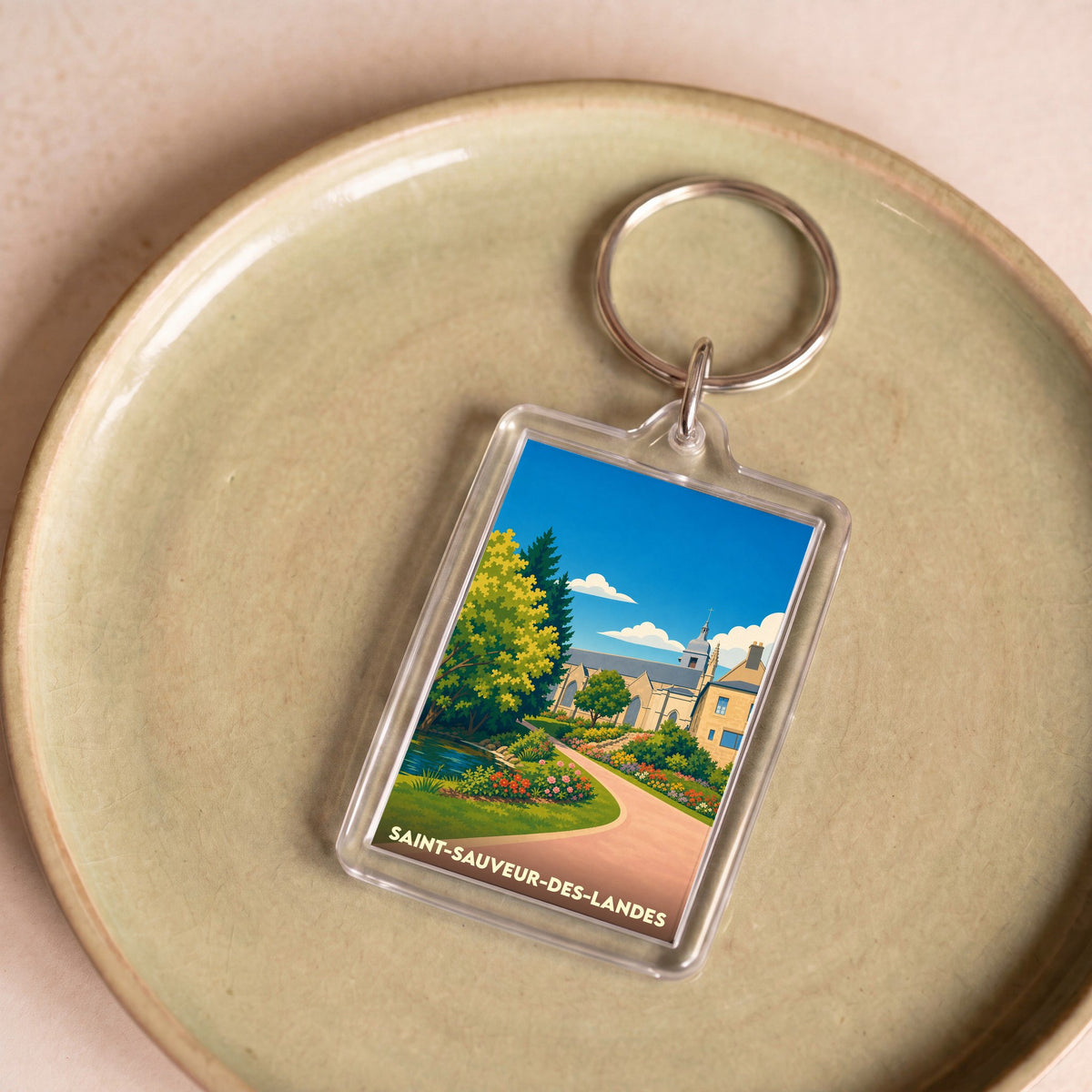 Porte-clés souvenir de la ville de Saint-Sauveur-des-Landes avec une illustration stylisée et colorée.