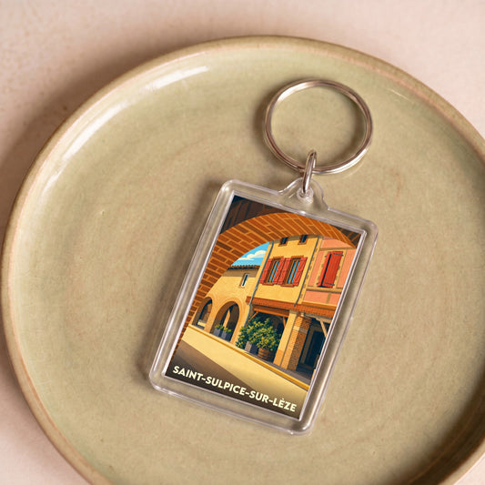 Porte-clés souvenir de la ville de Saint-Sulpice-sur-Lèze avec une illustration stylisée d'une rue pittoresque sous une arche.