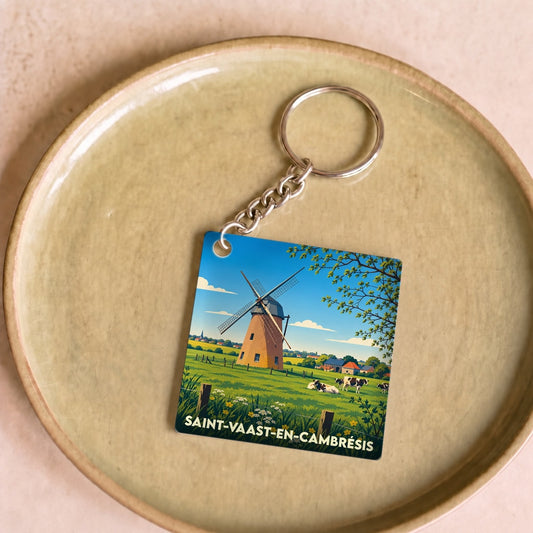 Porte-clés souvenir de la ville de Saint-Vaast-en-Cambrésis illustrant un moulin dans un paysage champêtre.