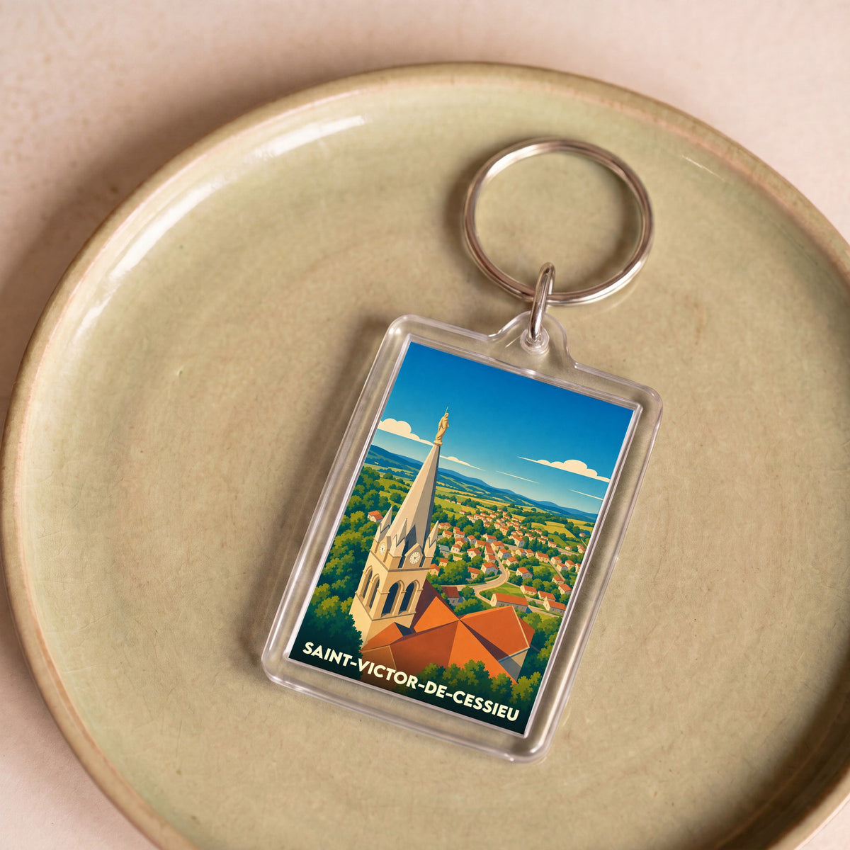 Porte-clés souvenir de la ville de Saint-Victor-de-Cessieu avec une illustration stylisée de son église et du paysage environnant.