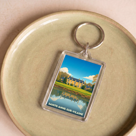 Porte-clés souvenir de Sainte-Anne-sur-Vilaine avec une illustration stylisée d'un manoir se reflétant dans l'eau.