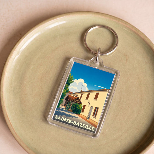 Porte-clés souvenir de la ville de Sainte-Bazeille avec une illustration stylisée d'un bâtiment ensoleillé.