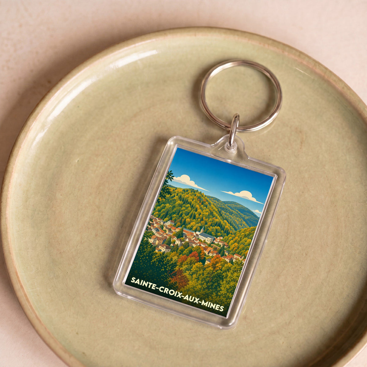 Porte-clés souvenir de la ville de Sainte-Croix-aux-Mines avec une illustration paysagère stylisée.