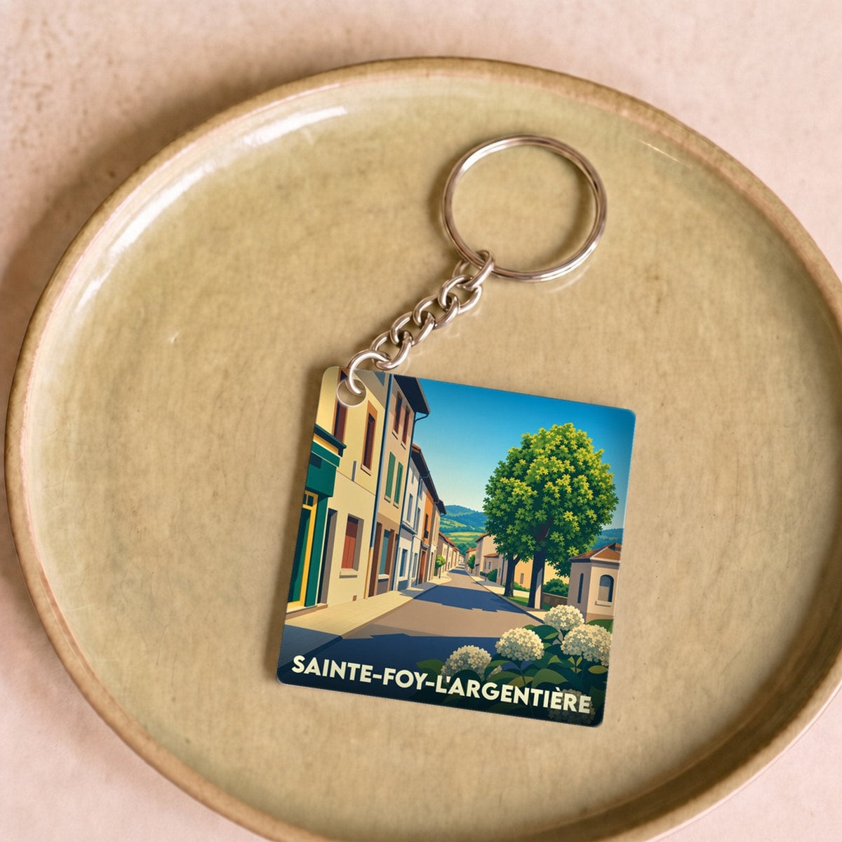 Porte-clés souvenir de la ville de Sainte-Foy-l'Argentière avec une illustration stylisée d'une rue ensoleillée.
