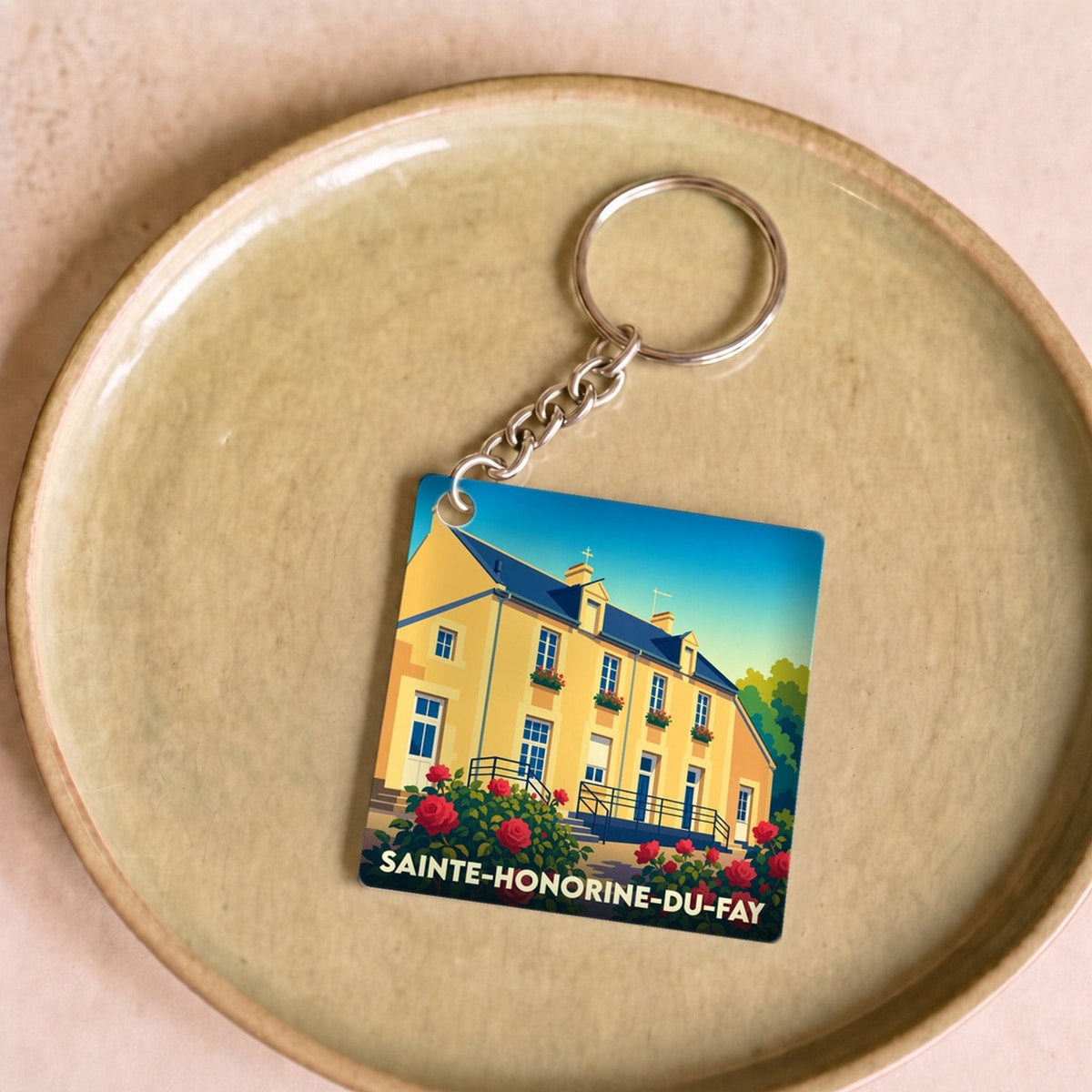 Porte-clés souvenir de la ville de Sainte-Honorine-du-Fay avec une illustration stylisée d'une maison fleurie.