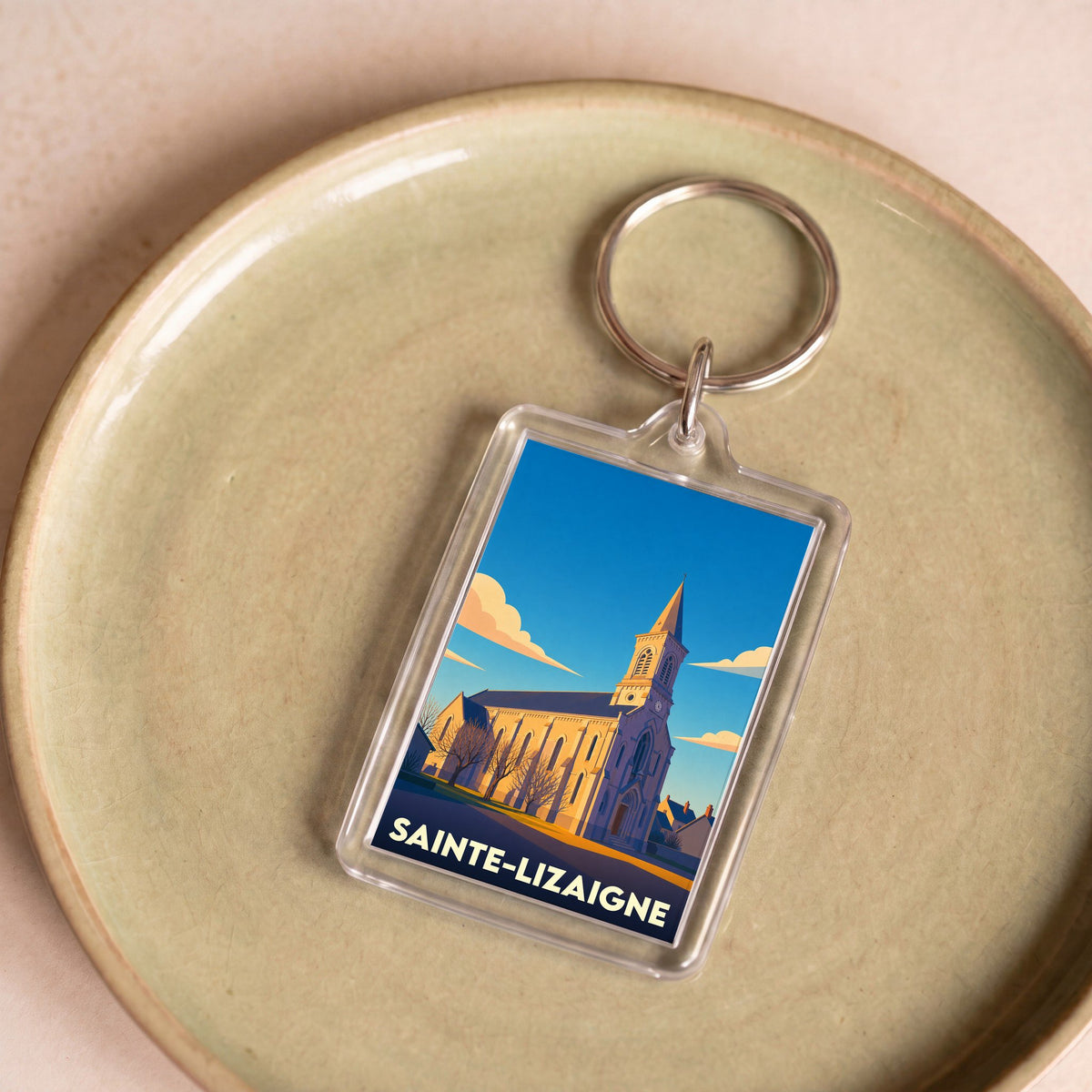 Porte-clés souvenir de la ville de Sainte-Lizaigne avec une illustration stylisée de son église sous un ciel bleu.