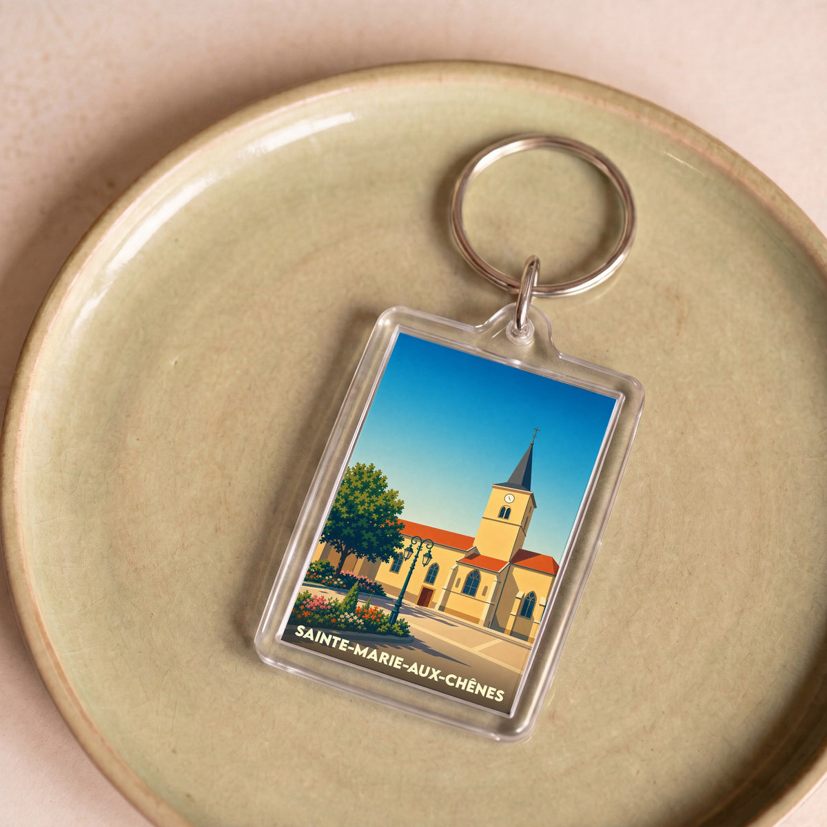 Porte-clés souvenir de la ville de Sainte-Marie-aux-Chênes avec une illustration stylisée de son église.