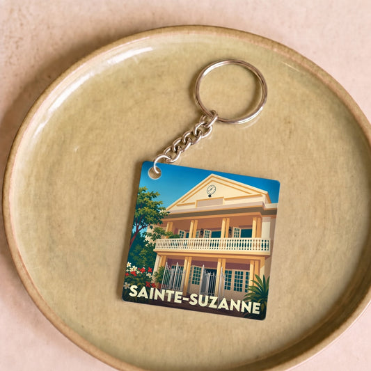 Porte-clés souvenir de la ville de Sainte-Suzanne avec une illustration stylisée d'un bâtiment historique.