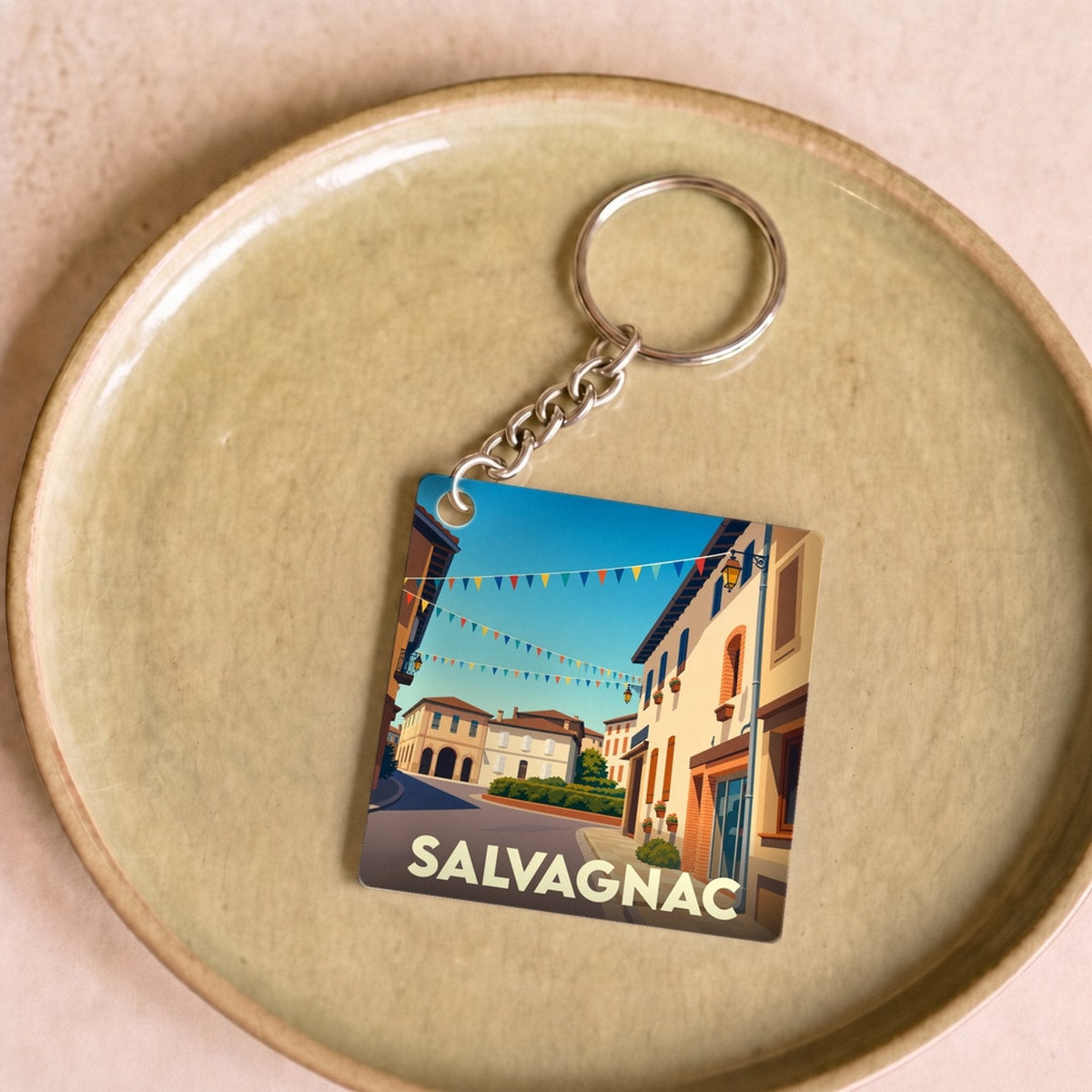 Porte-clés souvenir de la ville de Salvagnac avec une illustration stylisée d'une rue ensoleillée et pavoisée.