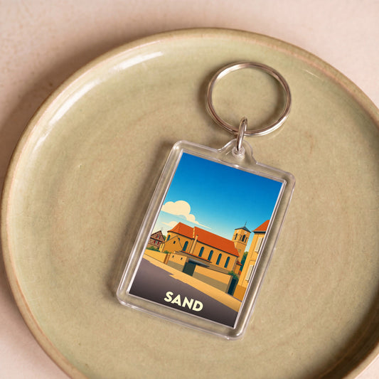 Porte-clés souvenir de la ville de Sand avec une illustration stylisée.