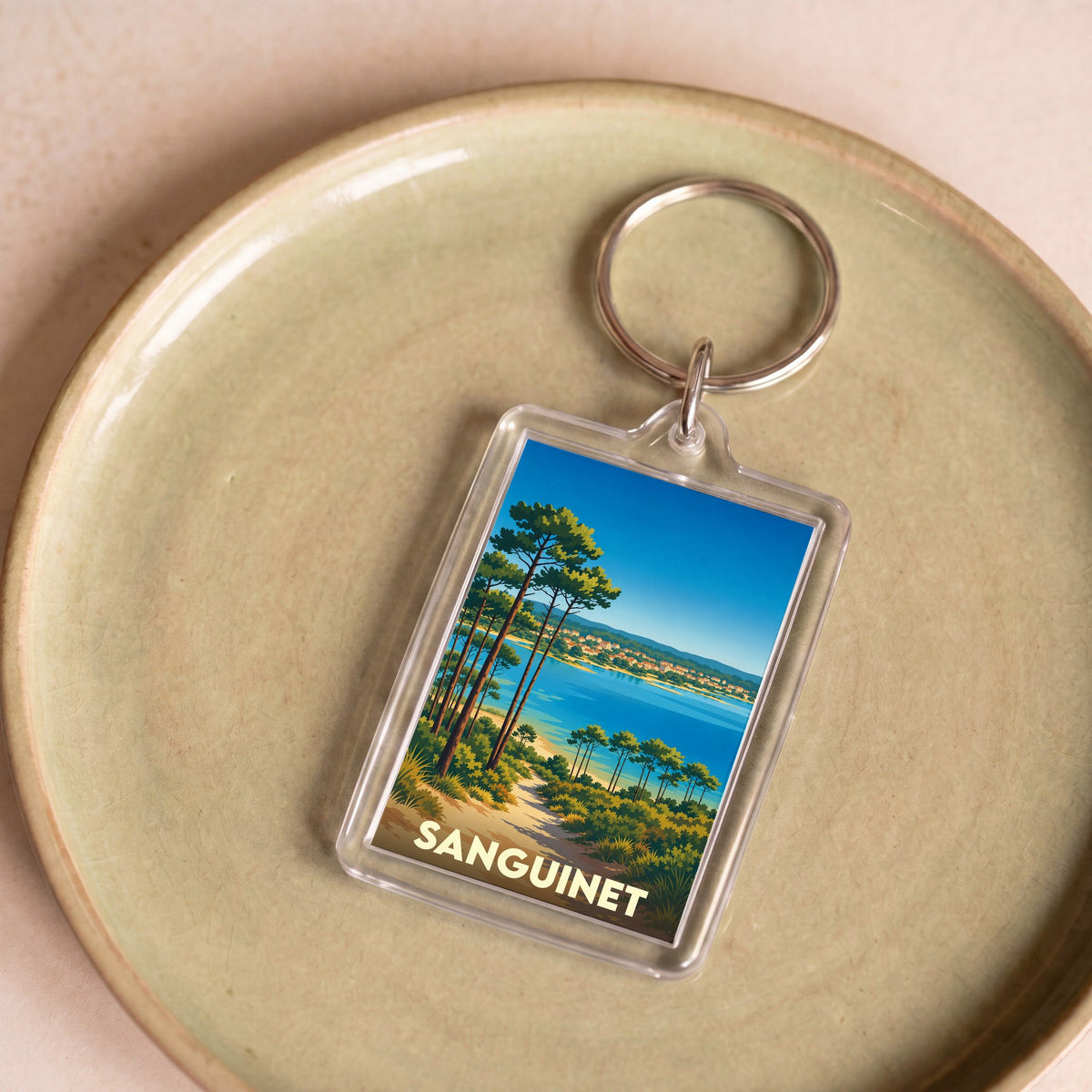Porte-clés souvenir de la ville de Sanguinet avec une illustration stylisée de son lac bordé de pins.